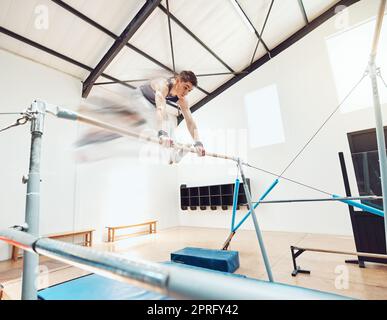 Gymnastics, olympics and sports with a gymnast swinging on a horizontal bar inside of a gym for fitness, training and workout. Sport, exercise and practice with an athlete holding onto parallel bars Stock Photo