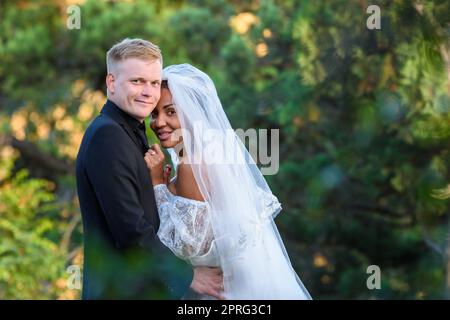 Portrait of young beautiful interracial newlyweds on green foliage background Stock Photo