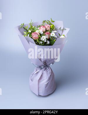 Delicate bouquet of roses wrapped in bright floral paper stands on a blue background. Stock Photo