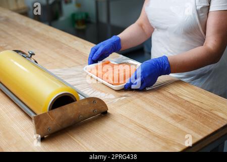 Worker in factory or shop packs raw fresh salmon fillets in cling film. Stock Photo