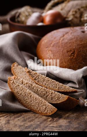 Sliced pieces of fresh rye black bread on lies on burlap on old wooden table. Stock Photo