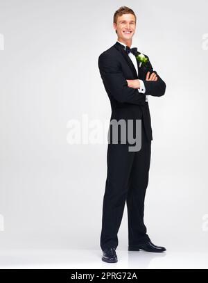 Wedding, marriage and groom with a handsome man standing arms crossed in studio against a white background. Happy male in a suit or tuxedo with a smile ready to get married at a celebration event Stock Photo