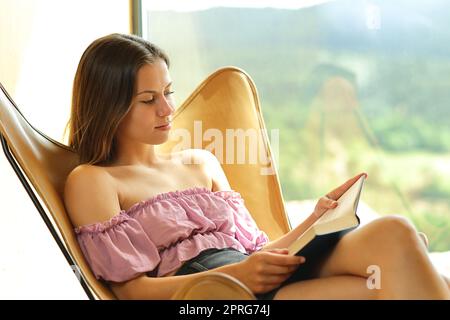 Relaxed woman reading book on a chair at home Stock Photo