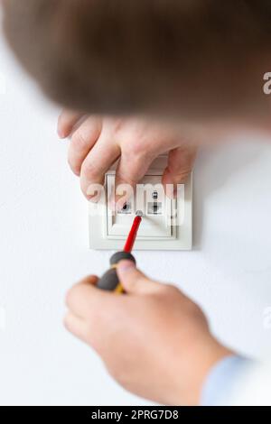 Electrician hands tighten bolts in wall fixture or socket using screwdriver. Stock Photo