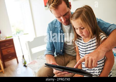 Teaching her about technology. a father and his young daughter sitting together in the living room at home using a digital tablet. Stock Photo