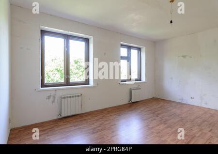 The interior of an empty room during renovation, there are two large windows in the room, radiators under them Stock Photo