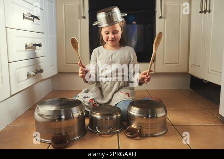 Shes a rock star in the making. a little girl playing drums on a set of pots in the kitchen. Stock Photo