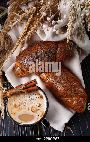 Fresh baked rolls with poppy seeds and coffee on rustic dark wooden table. Stock Photo