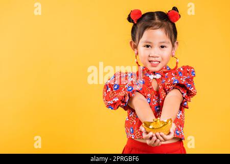 Happy Asian Chinese little girl smile wearing red cheongsam holding gold ingot Stock Photo