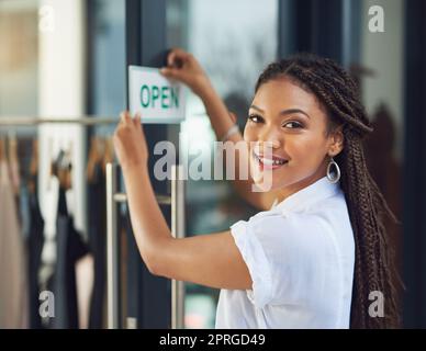 Ready for her customers. Portrait of a young business owner hanging up an open sign on the door of her shop. Stock Photo