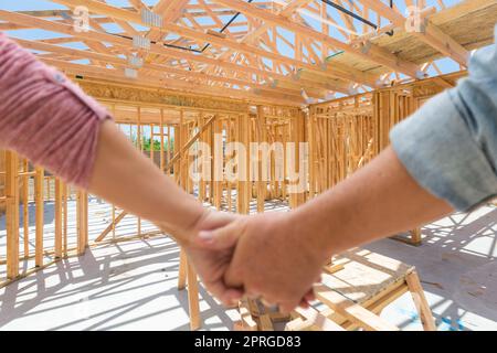 Couple Holding Hands Looking At Their New House Framing Under Construction. Stock Photo