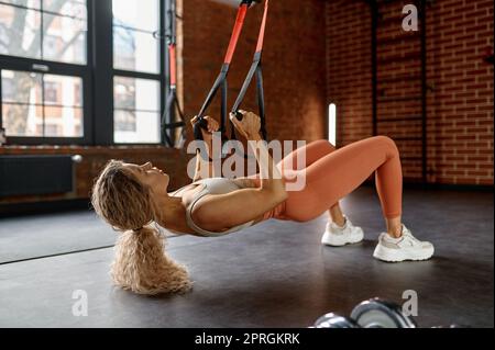 Young woman doing arm exercises with trx suspension straps at