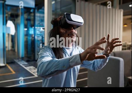 Zombie office worker using VR simulator headset. Undead monster businessman working with virtual reality futuristic technology Stock Photo