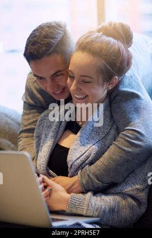 Lemme see that. an affectionate young couple surfing the net while relaxing on the sofa at home. Stock Photo