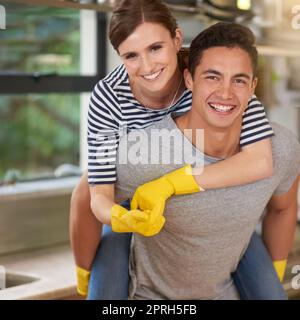 Who said spring cleaning had to be a chore. Portrait of happy young man giving his wife a piggyback ride while they clean their kitchen. Stock Photo