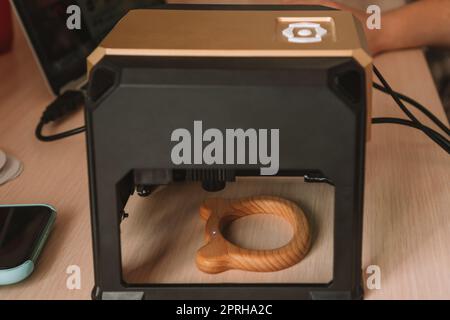 Desktop laser wood burning machine uses a blue laser beam to inscribe name on surface of childrens wooden toy. Home production of teethers and rattles Stock Photo