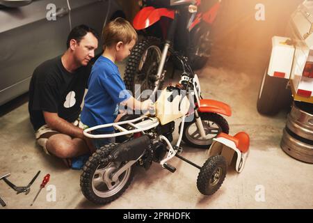 The boys are hard at work. a father and son fixing a bike in a garage. Stock Photo