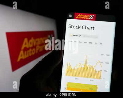 Person holding smartphone with website of US automotive company Advance Auto Parts Inc. on screen with logo. Focus on center of phone display. Stock Photo