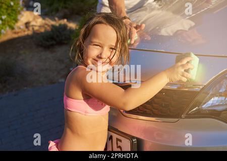 She loves helping. Portrait of a young girl having fun while washing a car with her father. Stock Photo