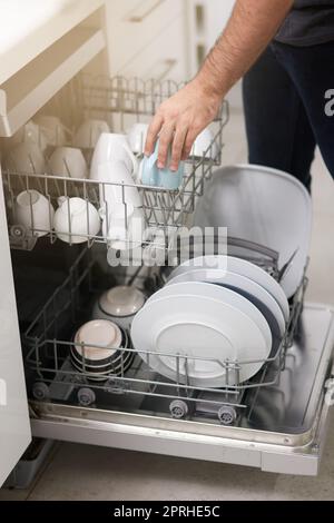 Keeping your dishes clean. a person loading a dishwasher at home. Stock Photo