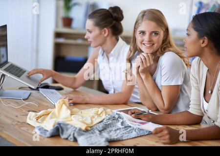 Happy with her success in the fashion world. Happy young fashion designers smiling at the camera with her two colleagues sitting next to her Stock Photo