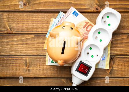 Electric socket, piggy bank and euro money on wooden table. Concept of increasing electric prices. Stock Photo