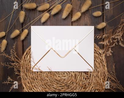 Blank paper envelope on wattled placemat near Hare's Tail grass top view, mockup Stock Photo