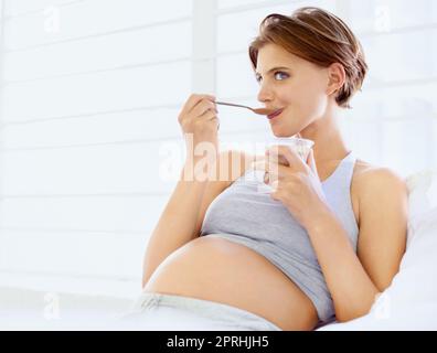 Enjoying a sweet treat. A happy young pregnant woman eating a small bowl of pudding Stock Photo