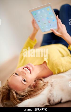 She finally found a tablet that was good for her health. A young woman laughing happily while lying on the floor holding a digital tablet Stock Photo