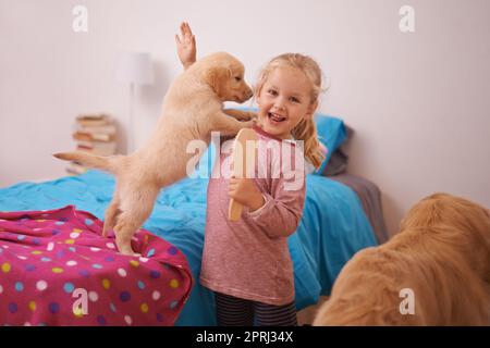 Look mom He jumped on me. A cropped shot of a little girl playing with her puppy in her bedroom Stock Photo