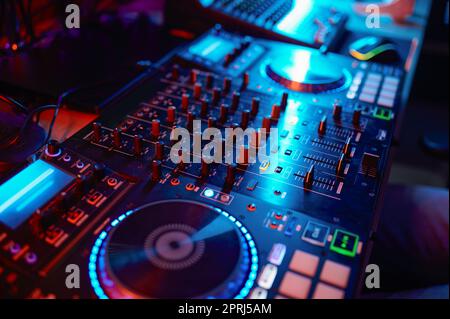Closeup on dj turntable in neon light, sound recording equipment knobs, music mixer Stock Photo