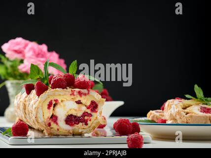 Baked meringue roll with cream and fresh red raspberry on a black ...