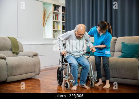 Asian nurse assisting helping senior man patient get up from wheelchair for practice walking Stock Photo