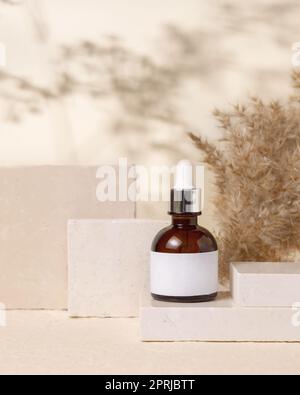 Brown dropper cosmetic bottle with blank label on stones near pampas grass close up, Mockup Stock Photo