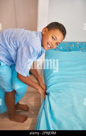 He keeps his room neat and tidy. Portrait of a young boy making up a bed. Stock Photo