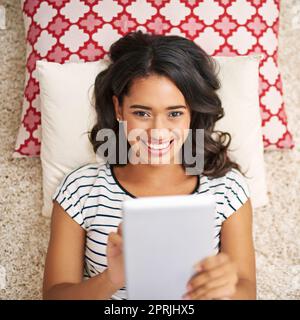 My social feeds are buzzing. High angle portrait of a young woman using her tablet while relaxing at home. Stock Photo