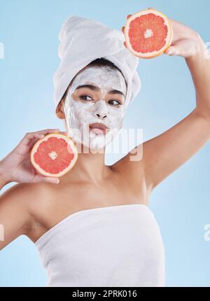 Skincare, health and face mask on a woman with a grapefruit doing an organic facial in studio. Girl with wellness, selfcare and healthy lifestyle doing a body care routine with tropical citrus fruit. Stock Photo