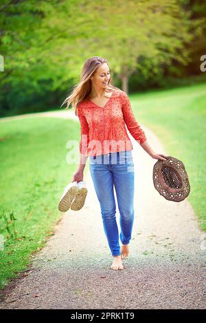 Green spaces are happy places. a young woman walking in a park holding her shoes and a hat. Stock Photo
