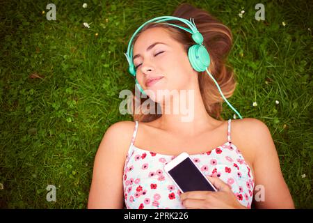 Find your freedom in the music. a young woman listening to music while lying on the grass. Stock Photo