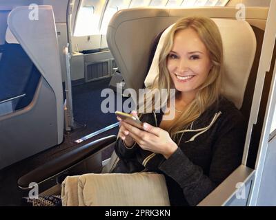 First class is the only way to go. Portrait of a young woman using her cellphone while sitting in first class in an airplane. Stock Photo