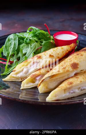 Thin pancakes stuffed with ham and melted cheese served with spinach, arugula, corn and chard salad Stock Photo