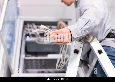 Internet network connection. Male technician's hand holds group of white network cables before connecting to port switch. Close up of plugs for intern Stock Photo