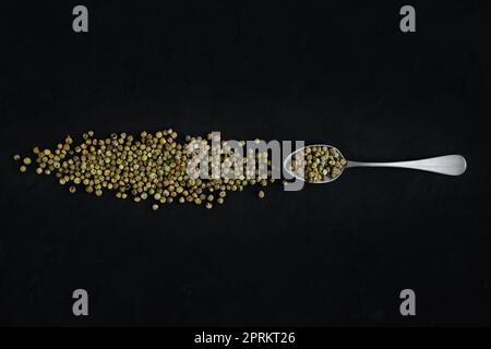 Dry green pepper scattered near metal spoon on dark background Stock Photo