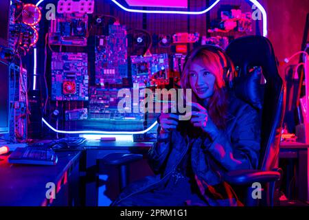 Gamer using joystick controller for virtual tournament plays online video game with computer neon lights, woman wear gaming headphones playing live st Stock Photo