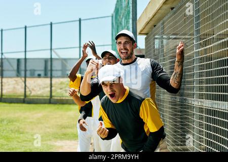 The game just keeps on getting better. a group of young baseball players cheering while standing near a baseball field during the day Stock Photo