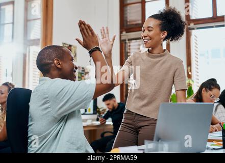 Thats why youre awesome to work with. a young businessman and businesswoman giving each other a high five while using a laptop in an office Stock Photo