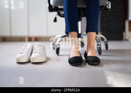 Pair Of A White Sport Shoes Besides Businesswoman's Legs In Office Stock Photo