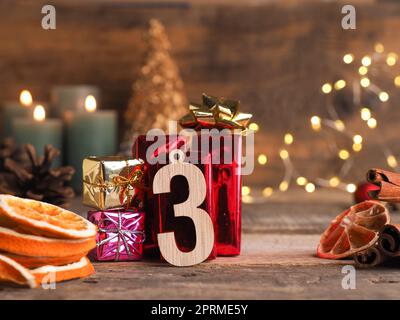 Candle of the third Advent burns, wooden number three with gift boxes, pine cones and Christmas decoration on wood with Christmas lights Stock Photo