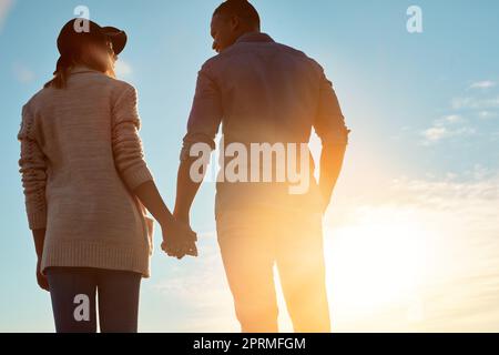 Lets spend every sunset together. Rearview shot of a happy young couple holding hands outdoors. Stock Photo