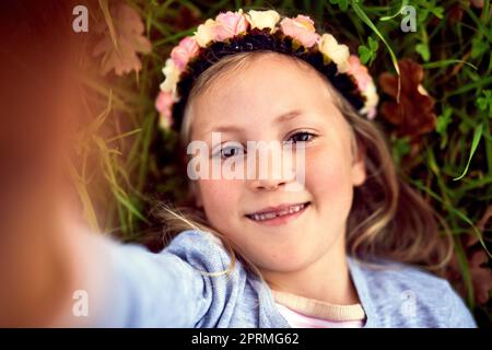 Shes one happy little kid. Portrait of a young girl taking a selfie while lying on the grass outside. Stock Photo